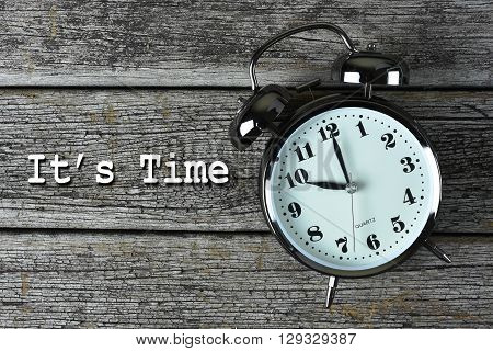 Black alarm clock on the rusty wooden table with word It's Time