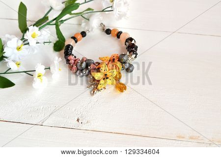 Beautiful female bracelet with stones, beads and flowers made of polymer clay on white wooden background with copy space for text