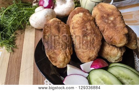 Fried cakes with potatoes, mushrooms and a dill on a black plate with radishes and cucumbers