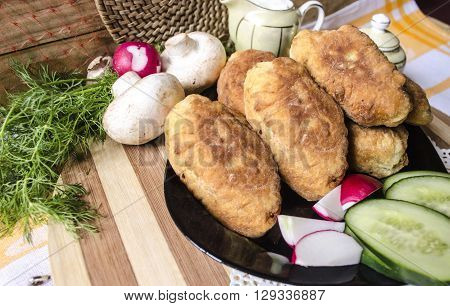 Homemade cakes with potatoes,mushrooms and a dill on a black plate with radishes and cucumbers