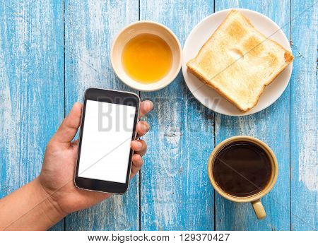 White display Smart phone in hand Toast Honey Coffee cup placed on blue wooden floor.