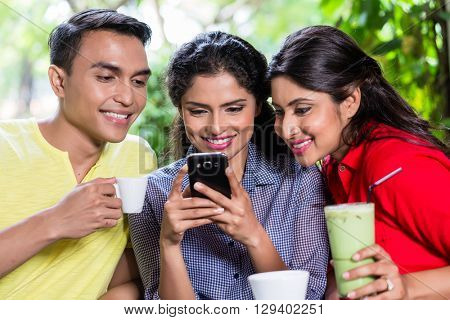Indian girl showing pictures on smart phone to her friends in an Indian cafe