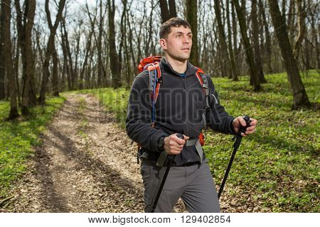 Active healthy man with red backpack hiking in beautiful forest.