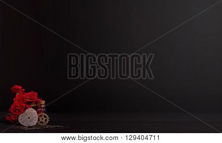 timeless heart next to the red ribbon roses, a cog wheel and glass bottle in the dark