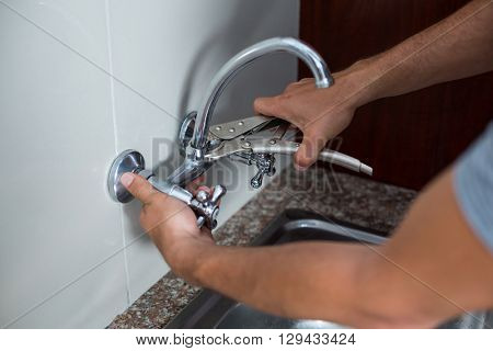 Cropped hands of man fixing faucet with wrench in kitchen