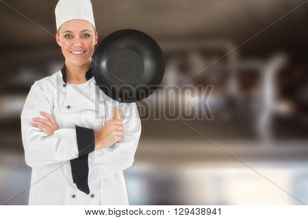 Female chef with arms crossed holds frying pan against large vats of beer