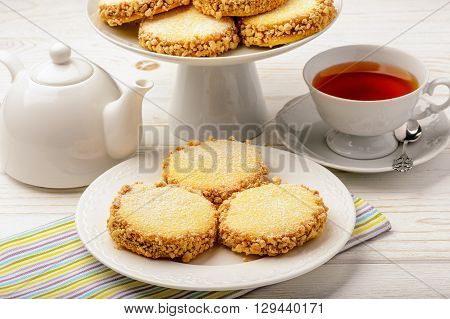 Butter cookies (alfajores) with caramel and peanut and cup of tea on wooden background.