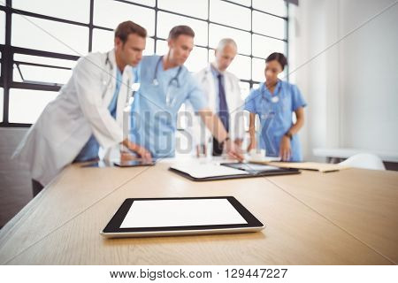 Digital tablet on table in conference room and medical team interacting in background