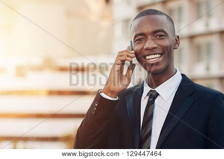 Portrait of a handsome young businessman of African descent talking on his mobile phone in a city while smiling broadly at the camera