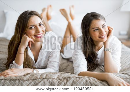 Two beautiful girls talking and smiling while lying on a luxorious bed