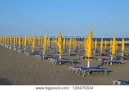 Yellow Closed Sun Umbrellas On Sea Beach With Sun Loungers