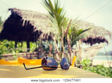 Sunglasses lying on a yellow table in a tropical beach cafe. Vacation theme concept