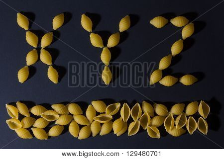 alphabet laid out in the form of pasta shells on a dark background . XYZ