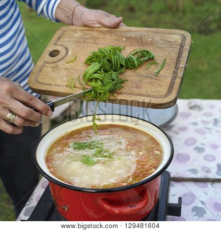 Hand of a cook sweeping chopped green pepper into a vegetarian soup cooking on a hotplate