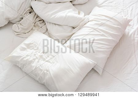 Top view of an unmade bed in a bedroom with crumpled bed sheet a blanket a white shower towel and two pillows after waking up in the morning. Not having bedclothes neatly arranged for sleep in.