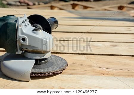 Front part of angle grinder with abrasive disc on planks after work.