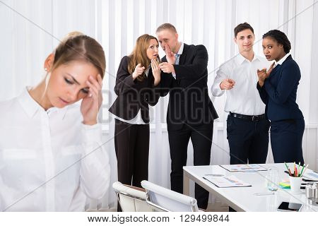 Businesspeople Gossiping Behind Stressed Female Colleague In Office