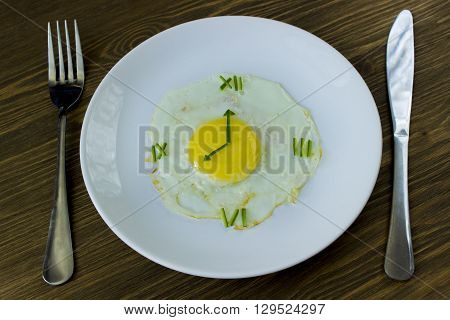 Fried egg in form of a clock with fork and knife