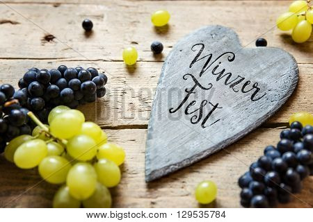 Blue and white grapes and a wooden heart with german word Winzerfest on it which means wine festival