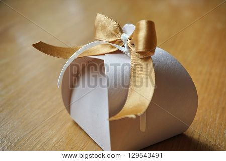 Small gift box made of paper with a colorful ribbon topnot atop on a wooden background
