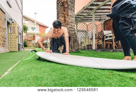Portrait of surfer man with wetsuit waxing surfboard of a beautiful woman. Summer sports concept.