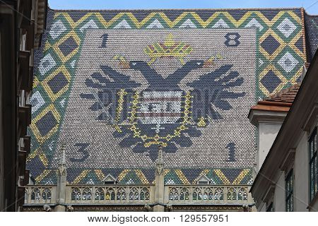 VIENNA AUSTRIA - JULY 12: Coat of Arms at St. Stephen Cathedral in Wien on JULY 12 2015. Side View of Stephansdom Basilica With Sign at Roof Tiles in Vienna Austria.
