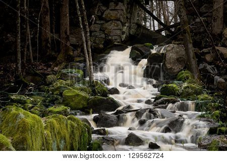 Small waterfall with green moss on rocks. water running through old stonewall