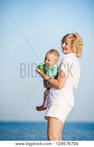 Mother with toddler walking on the beach in summer. Happy mother holding a baby in her arms and walks along the beach in the summer.