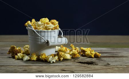 White bucket with popcorn on wooden background