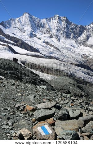 White and blue trail sign painted on a Rock. Saas-Fee. Swiss Alps