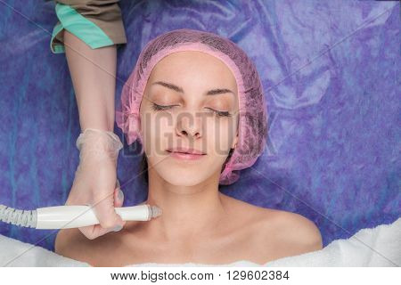 Beautician cleans the client skin before applying the cosmetic mask for the face. Closeup portrait of lovely happy young woman with hands holding medical maniples touching her face in Beauty salon.