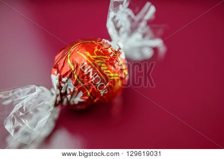 KILCHBERG SWITZERLAND - MARCH 20 2014: Tasty Lindt Lindor chocolate truffle on a red luxury silk background. Lindt is one one of the lastgest luxury chocolate and confectionery company worldwide with more than 30 factories worldwide