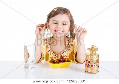 Young Muslim girl eating dates for brakfast in Ramadan - sitting on a table with water dates Quran and Ramadan lantern