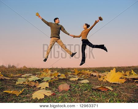 jump couple. autumn leaves. sunset sky