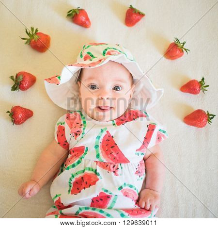 A baby girl in a melon print set is laying on a bed or Berry Baby or Strawberry Baby