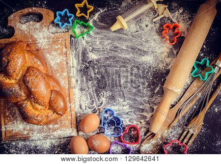 Baking concept on dark background. Baking cookies for children top view of variety of baking utensils with bread eggs and colorful cutters on black chalkboard. Children cooking. Top view.