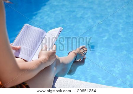Girl reading a book by the swimming pool