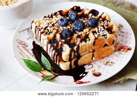 Belgian waffles with peanut chocolate sauce and blueberry, bilberry, whortleberry, huckleberry, hurtleberry, blaeberry on a plate in still life straw