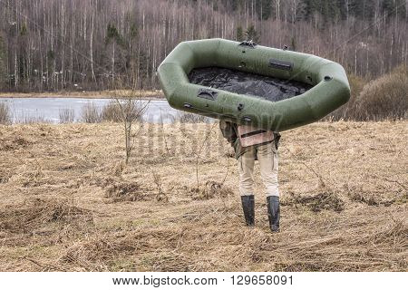 man carries a rubber inflatable boat on the shore of the lake located near the forest in order to go fishing