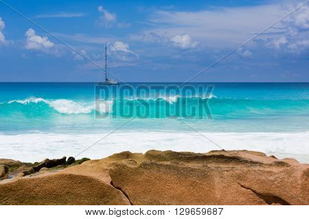 Seychelles beach with granite rock, turquoise water with sailing ship