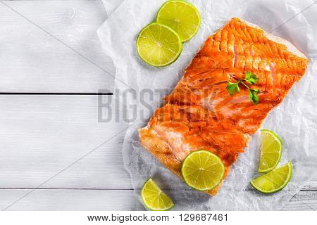 Delicious red fish salmon steak fillet on a white parchment paper with lime slices on a wooden table blank space left studio lights top view