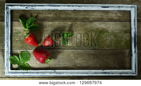 Strawberries in the old frame on a wooden background