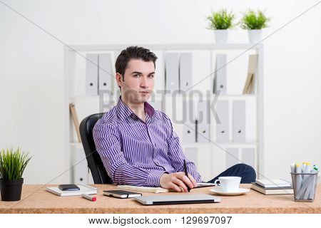 Caucasian businessman sitting at desk with various items in office and looking at the camera
