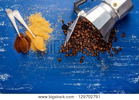 Arabika beans in moka pot, brown sugar and ground coffee in spoons on wooden blue painted table. Top view, copy space