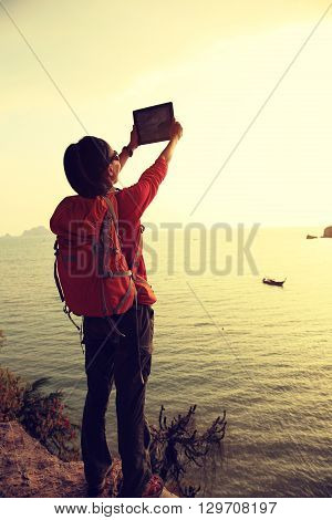 young woman hiker use digital tablet on sunset seaside