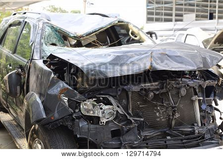 A wrecked car lays in wait after a vicious car accident. Rescue workers linger in the background.