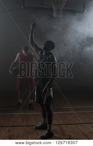 Victorious basketball player raising his arms up while his rival looking down