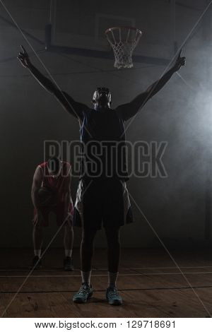 Victorious basketball player raising his arms up while his rival looking down