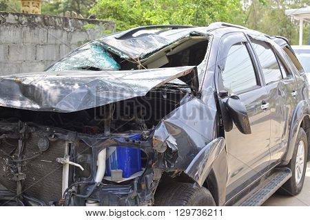 A wrecked car lays in wait after a vicious car accident. Rescue workers linger in the background.