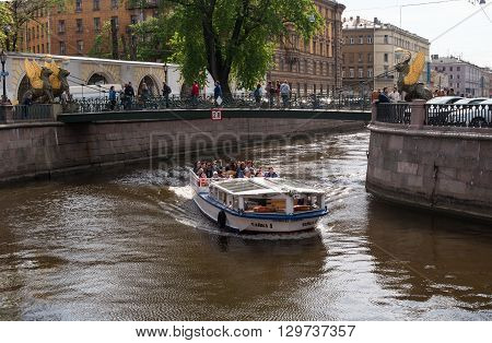 St. Petersburg, Russia - May 14, 2016: Tourist boat on the Griboyedov Canal. The ship sails under the Banking bridge. Bank Bridge decorated Griffon - lions with golden wings.